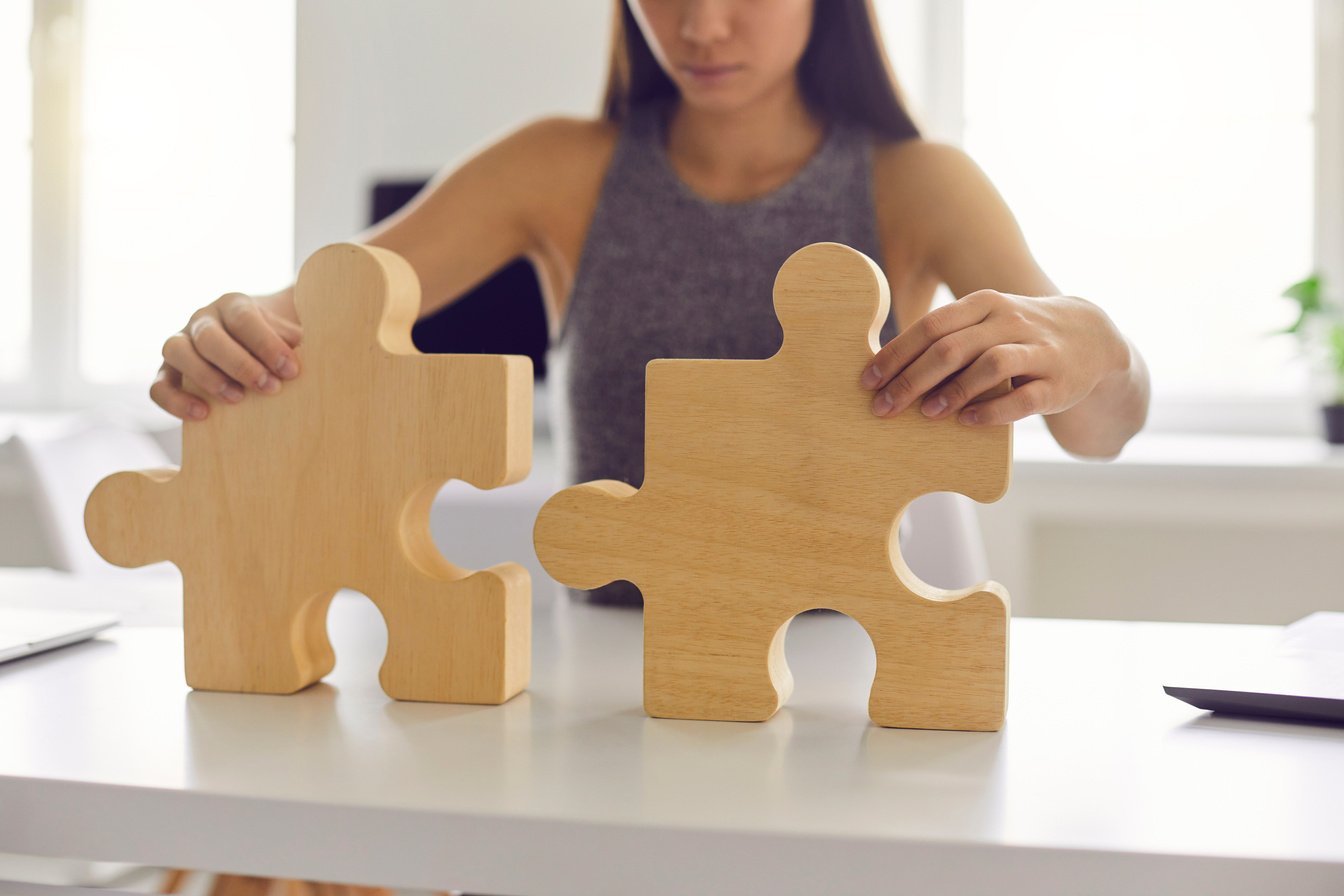 Business Woman Standing and Trying to Make Whole Picture from Wooden Details Puzzle Alone in Office